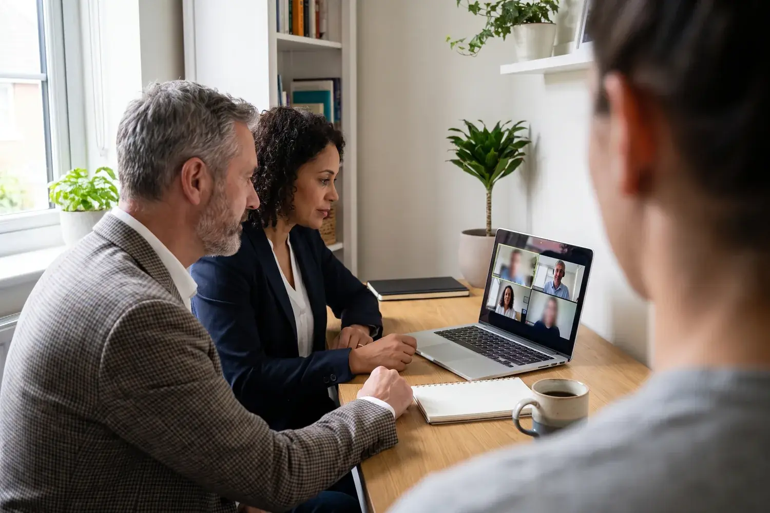 Two executives in a small office join a video call with a customer on a laptop